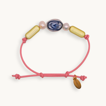 A pink cord bracelet with a sliding knot closure, decorated with a blue and white agate bead, two pink freshwater pearls, and two gold capsule beads. A small gold tag attached to the cord.