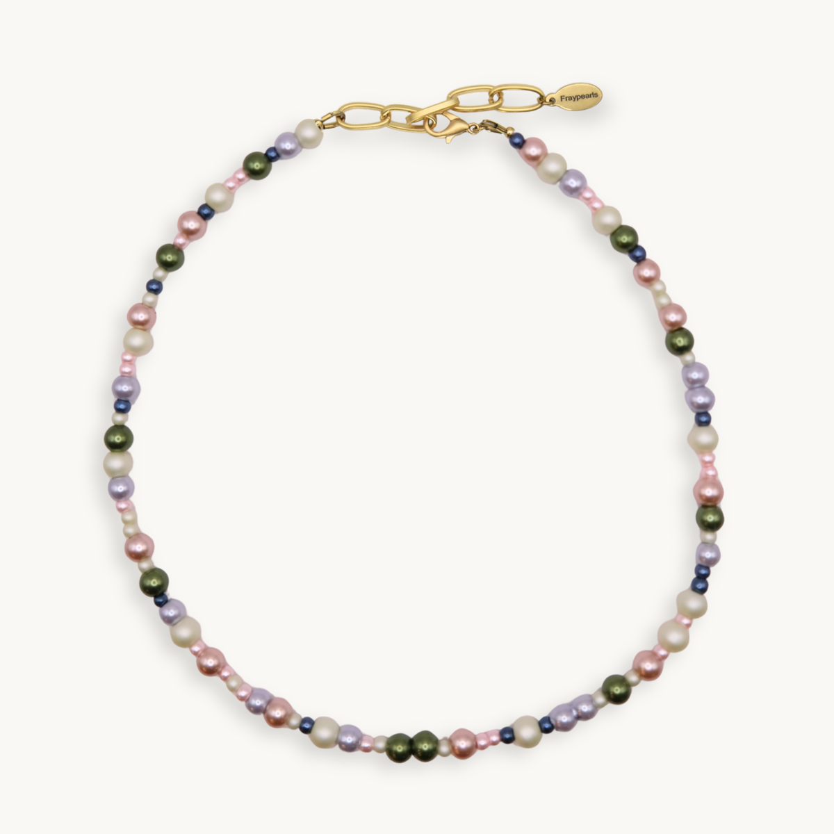 A delicate beaded necklace featuring a mix of freshwater pearls in pink, cream, and olive green, accented with small dark blue beads, finished with a gold-tone lobster clasp on a light cream background.