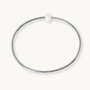 A minimalist polished silver-tone bangle bracelet with a single small white pearl bead at the top, shown on a clean off-white background.