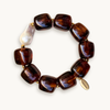 Brown gemstone bracelet with square beads, featuring a single irregular white pearl. Gold accents add elegance against a plain white background.