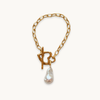 Gold chain bracelet with large links, featuring a toggle clasp in a flower shape, and a dangling teardrop-shaped pearl, creating an elegant look.