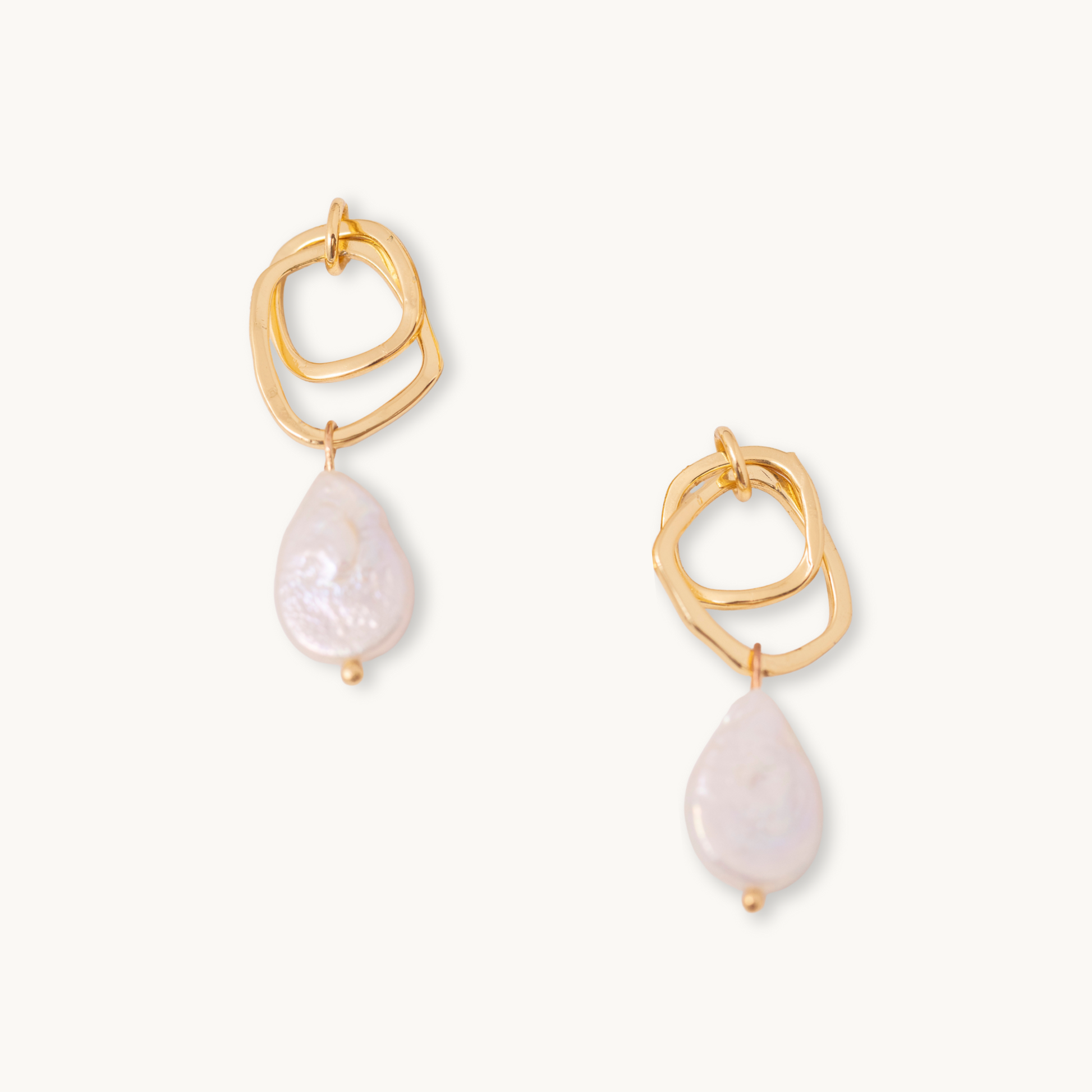 Elegant drop earrings with geometric gold loops and teardrop-shaped white pearls. The style is minimalist and sophisticated, set against a plain background.