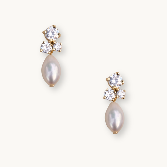 Gold stud earrings feature three sparkling diamonds and a dangling teardrop pearl. The elegant design conveys luxury and sophistication.