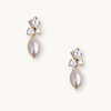 Gold stud earrings feature three sparkling diamonds and a dangling teardrop pearl. The elegant design conveys luxury and sophistication.