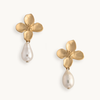 Gold flower-shaped earrings with white teardrop pearls dangling beneath, set against a plain background. They convey a sense of elegance and sophistication.