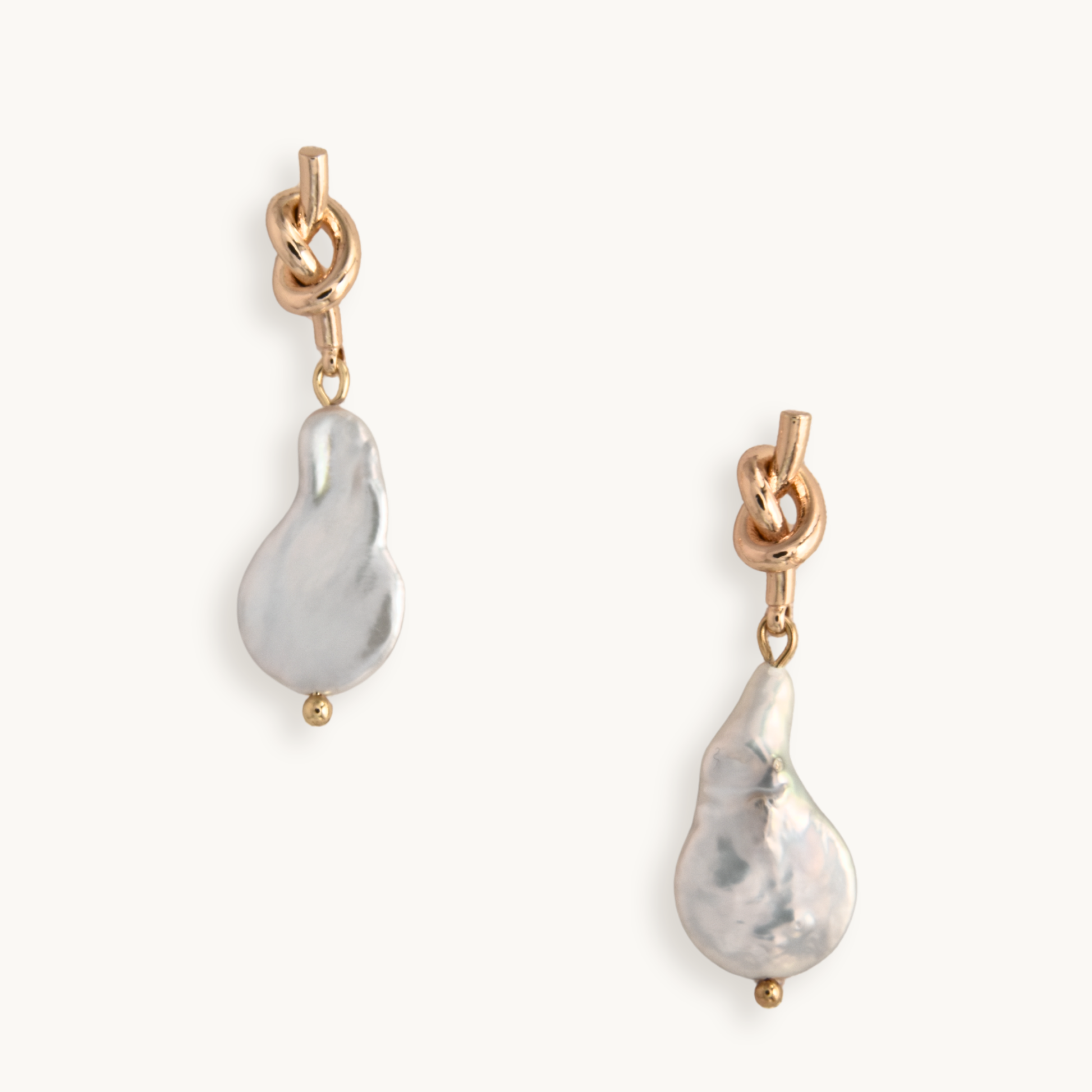 Gold earrings feature a unique knotted design with dangling baroque pearls, creating an elegant and artistic look against a plain white background.
