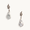 Silver earrings feature a unique knotted design with dangling baroque pearls, creating an elegant and artistic look against a plain white background.