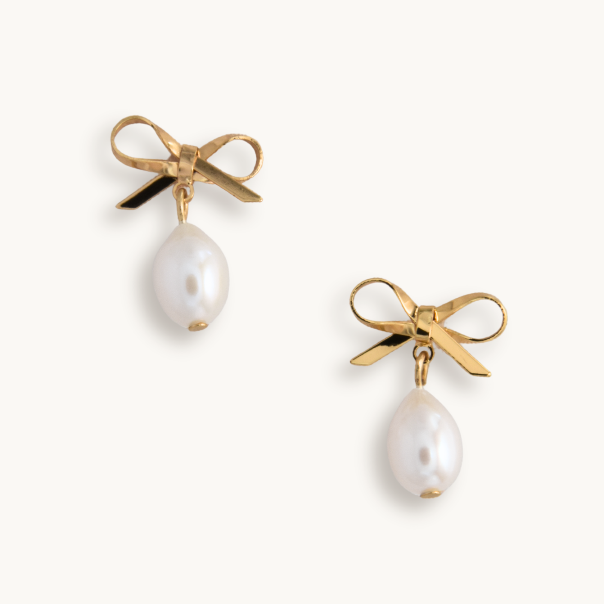 Pair of earrings with gold bows and pearl drops on a white background