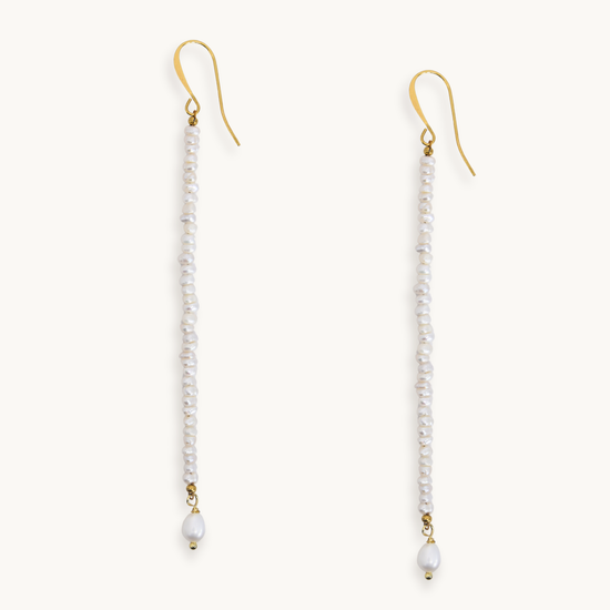 A pair of long drop earrings with gold fishhook wires, small white pearls, and a larger white bead dangling at the bottom, shown on a plain light background.