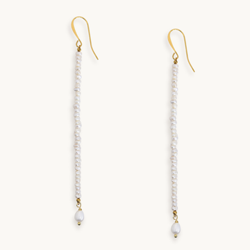 A pair of long drop earrings with gold fishhook wires, small white pearls, and a larger white bead dangling at the bottom, shown on a plain light background.