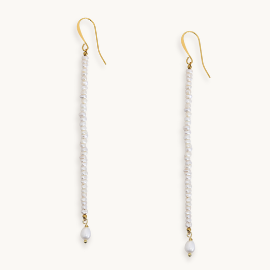 A pair of long drop earrings with gold fishhook wires, small white pearls, and a larger white bead dangling at the bottom, shown on a plain light background.