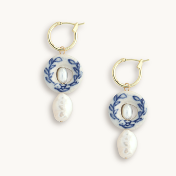 Gold hoop earrings with dangle elements including a white circle with blue florals, surrounding a small pearl