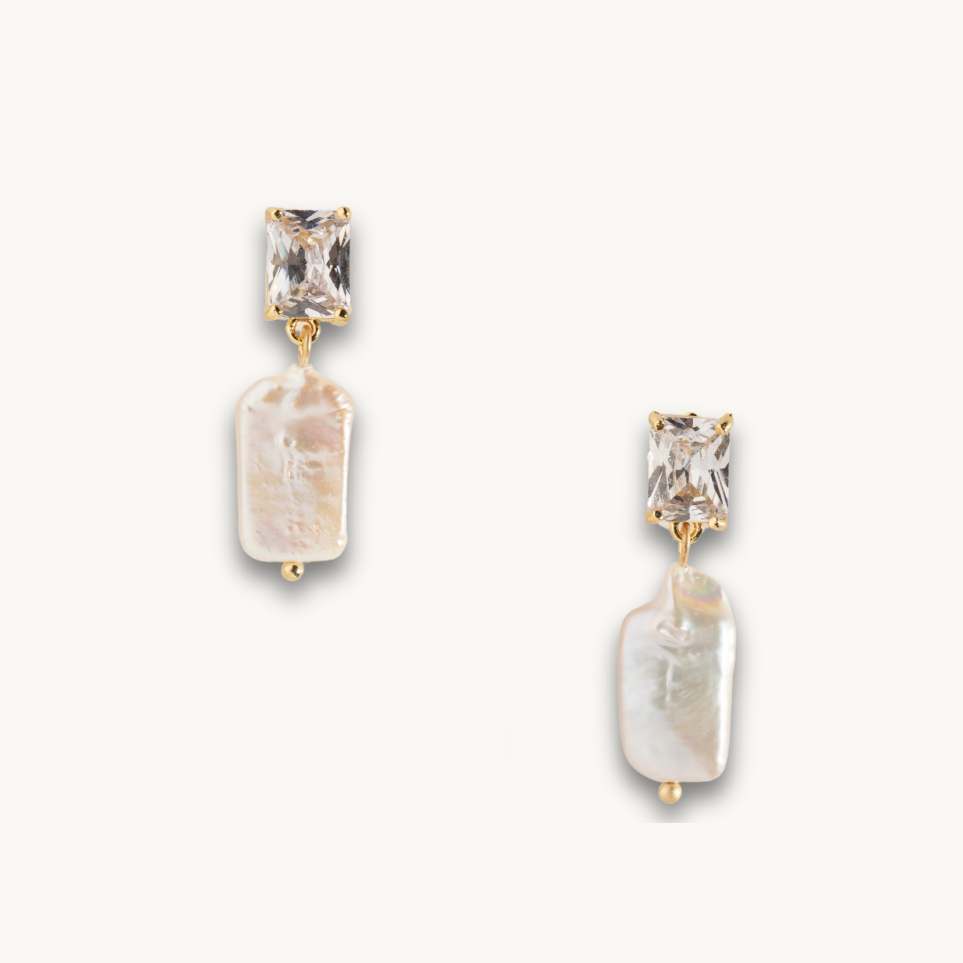 Gold earrings with a rectangular clear gemstone on top and an irregularly shaped white pearl below, set against a plain white background.