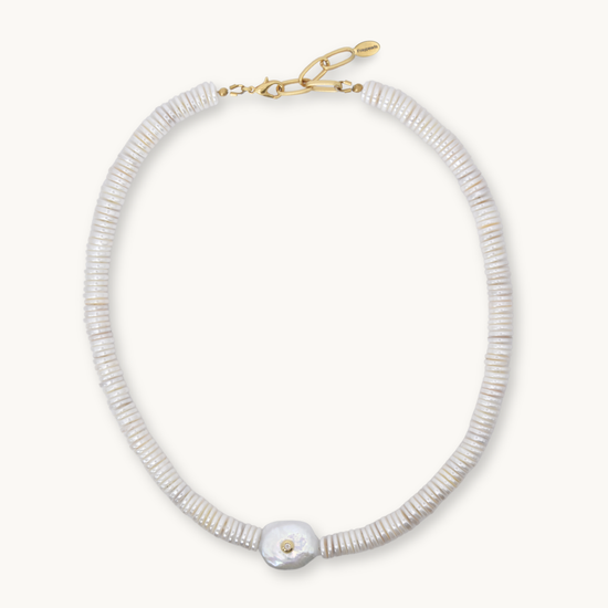 A delicate necklace made of small, tightly packed white beads with a single larger white shell pendant and a gold clasp, shown on a light cream background.