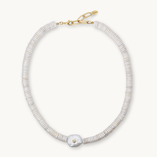 A delicate necklace made of small, tightly packed white beads with a single larger white shell pendant and a gold clasp, shown on a light cream background.