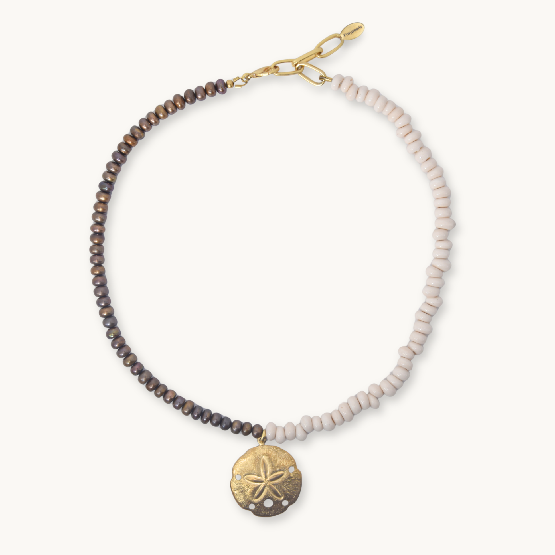 A beaded bracelet with a split design of dark brown and light pinkish-beige beads, featuring a gold-tone lobster clasp and a textured gold-tone sand dollar pendant, shown on a light cream background.