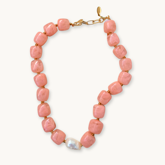 A necklace with pink, cube-shaped beads linked with small gold beads and a single large white pearl. The piece has a gold clasp and exudes elegance.