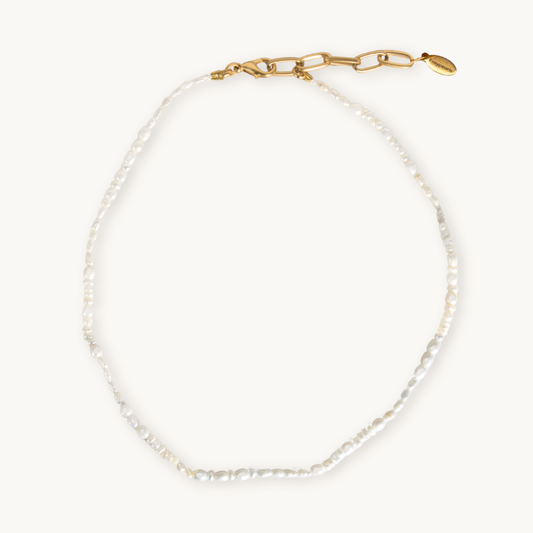 A delicate pearl necklace with irregularly shaped white pearls arranged in a circle on a plain white background, conveying elegance and simplicity.