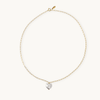 A delicate gold chain necklace with an elongated link design, featuring a shiny heart pearl pendant at the center, against a plain light background.
