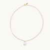 A delicate gold chain necklace with an elongated link design, featuring a shiny round pearl pendant at the center, against a plain light background.