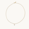 A delicate gold chain necklace with an elongated link design, featuring a shiny teardrop pearl pendant at the center, against a plain light background.