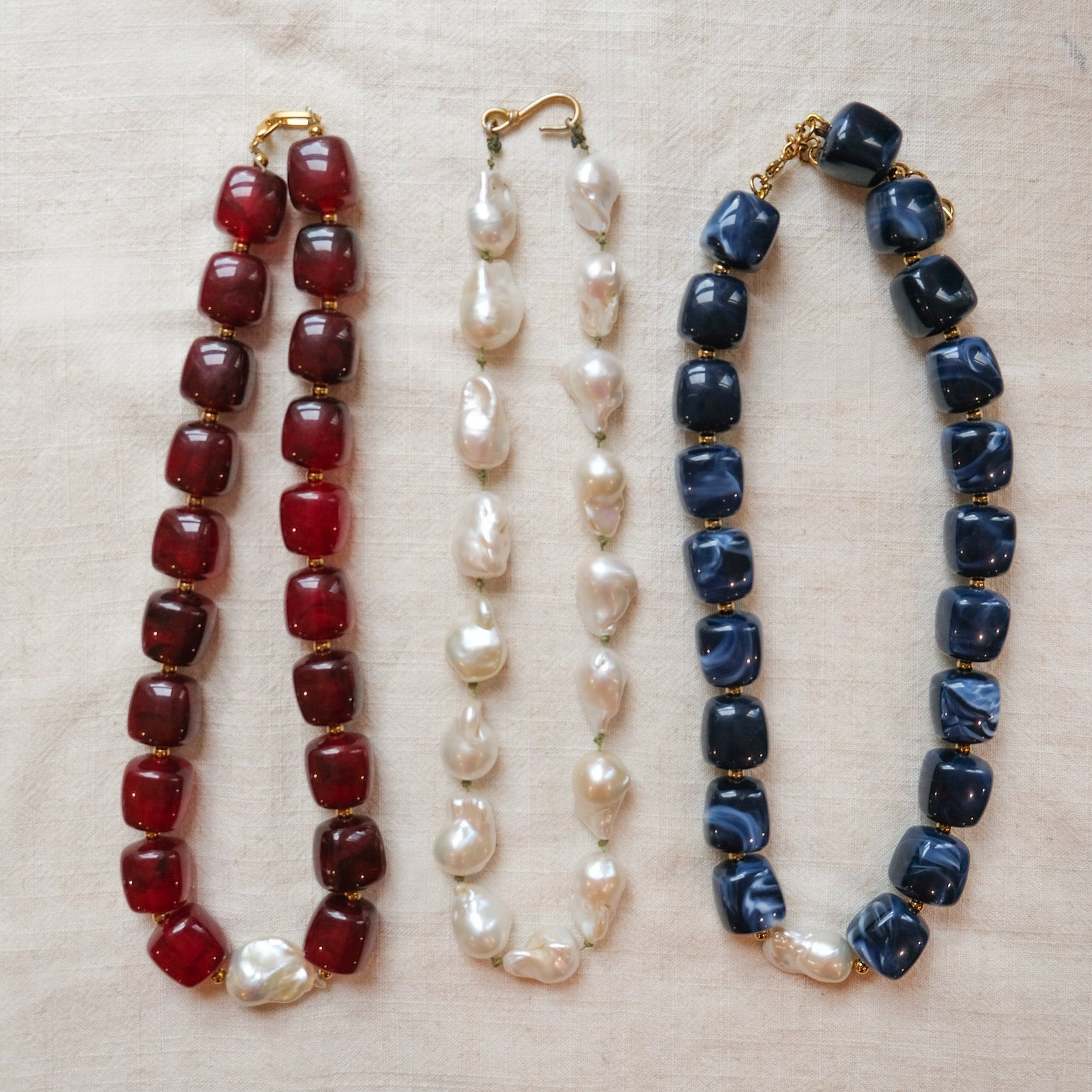 Three necklaces with different colored beads on a beige fabric background