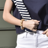A close-up of a person's torso showcasing a navy shirt, white pants, and a striped sweater draped over one shoulder. The person wears a chunky beige bead and pearl bracelet.