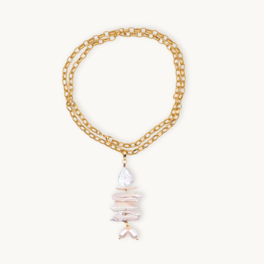 A long gold necklace features an elegant pendant with stacked irregular pearls in shades of white, creating a sophisticated and organic aesthetic.
