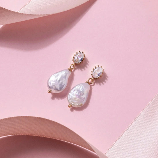 Elegant pearl drop earrings with gold accents and sparkling oval gems, set against a soft pink background, convey luxury and sophistication.