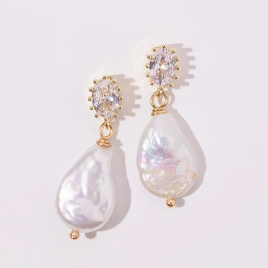 Elegant pearl drop earrings with gold accents and sparkling oval gems, set against a soft white background, convey luxury and sophistication.