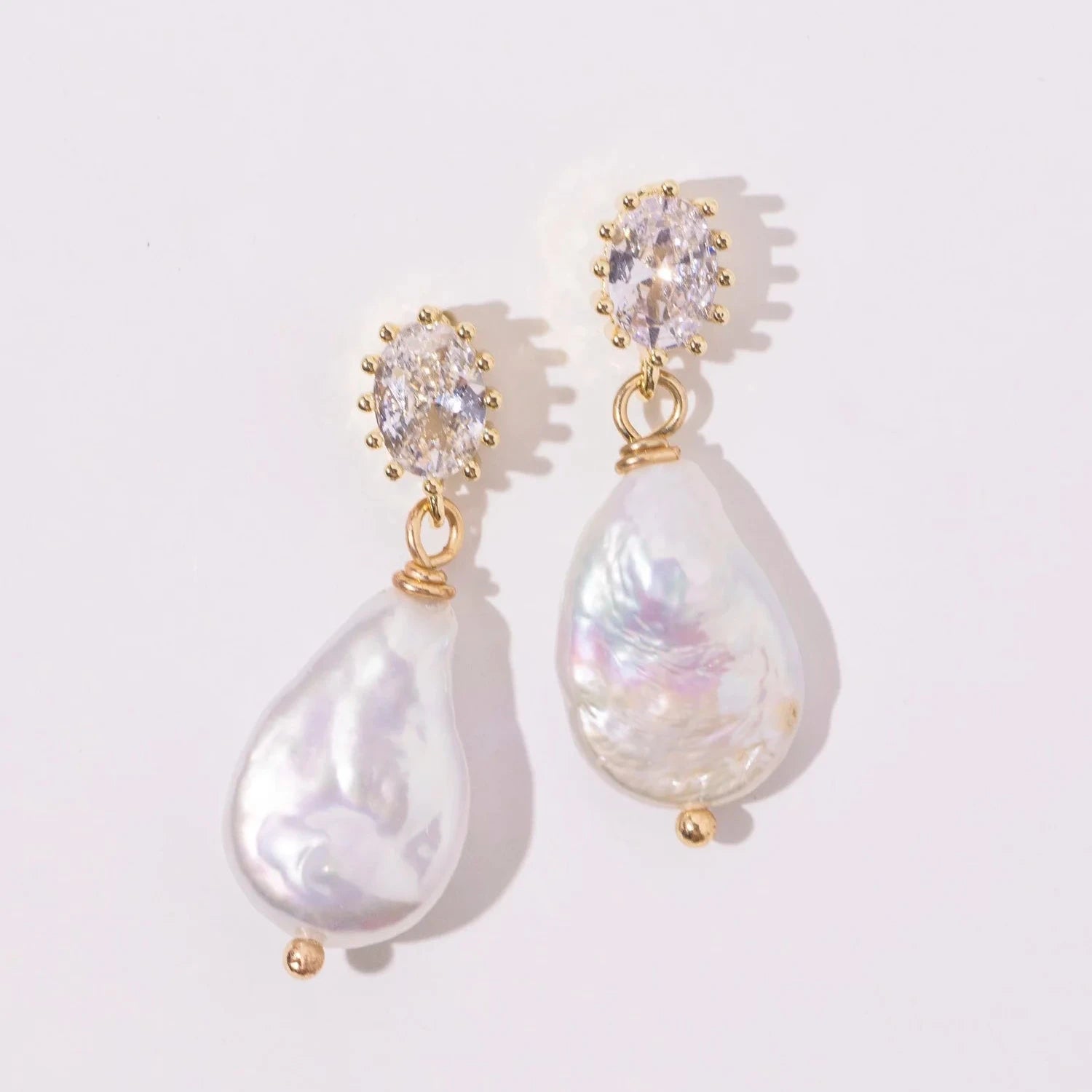Elegant pearl drop earrings with gold accents and sparkling oval gems, set against a soft white background, convey luxury and sophistication.