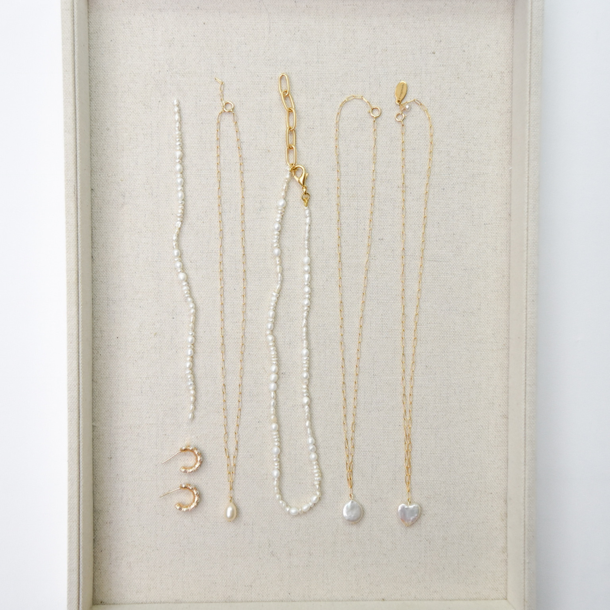 Elegant jewelry display with delicate gold chains and pearl accents lies on a beige fabric background, creating a sophisticated and minimalist aesthetic.
