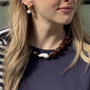 Woman wearing gold and pearl earrings, a chunky brown bead necklace with a large, irregular white pearl, against a navy top and striped sweater.