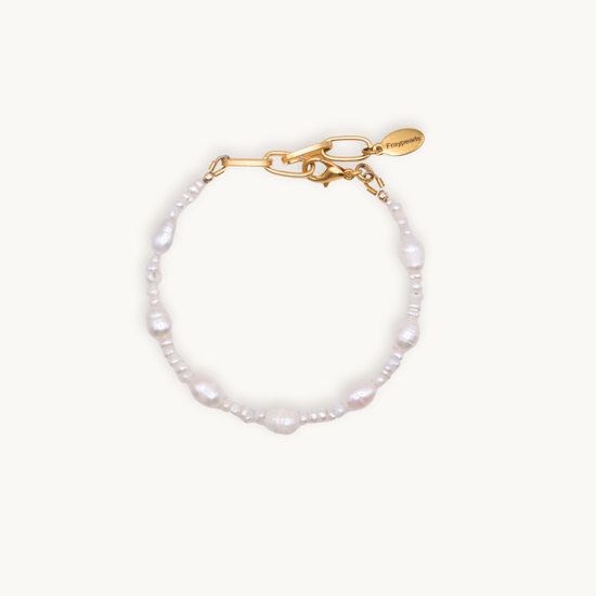 A delicate bracelet with irregular white pearls and small beads, featuring a gold chain and clasp with a small tag. It conveys elegance and simplicity.