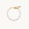 A delicate bracelet with irregular white pearls and small beads, featuring a gold chain and clasp with a small tag. It conveys elegance and simplicity.