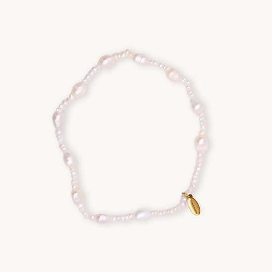 A delicate white pearl bracelet featuring irregularly shaped beads and a small gold tag with engraved text. The tone is elegant and timeless.