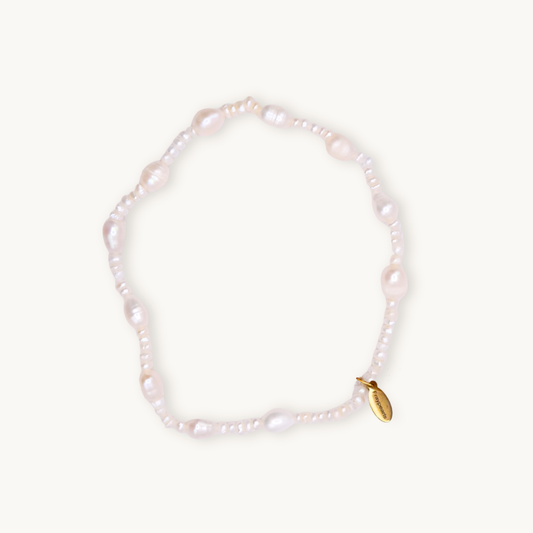 A delicate white pearl bracelet featuring irregularly shaped beads and a small gold tag with engraved text. The tone is elegant and timeless.