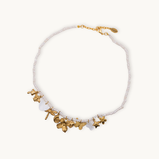 Delicate beaded necklace with subtle white beads and gold charms including a mushroom, flower, and dragonfly. The tone is whimsical and elegant.