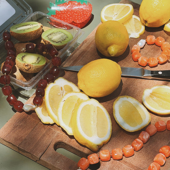 Lemons and kiwi slices on a wooden board, surrounded by colorful beaded bracelets. Sunlight casts soft shadows, creating a warm, fresh tone.
