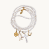 A wrap necklace of white irregular pearls featuring four charms: a gold clover, a fish, a cross, and a horseshoe, each with intricate details.