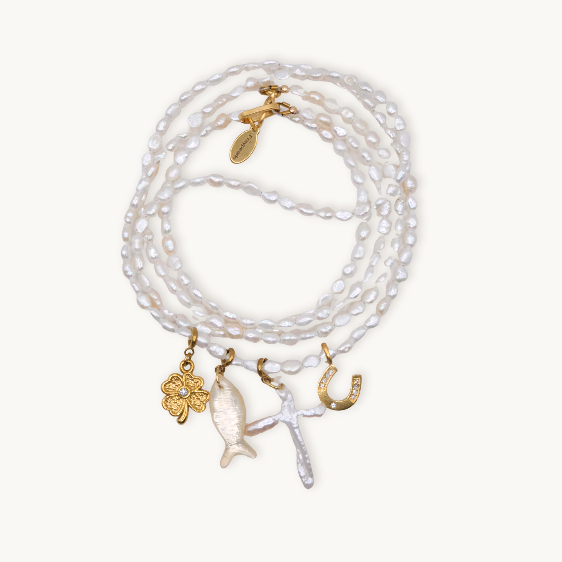 A wrap necklace of white irregular pearls featuring four charms: a gold clover, a fish, a cross, and a horseshoe, each with intricate details.