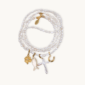 A wrap necklace of white irregular pearls featuring four charms: a gold clover, a fish, a cross, and a horseshoe, each with intricate details.
