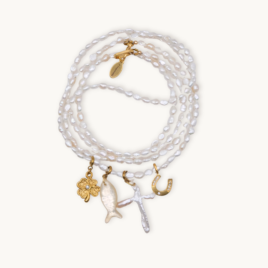 A wrap necklace of white irregular pearls featuring four charms: a gold clover, a fish, a cross, and a horseshoe, each with intricate details.