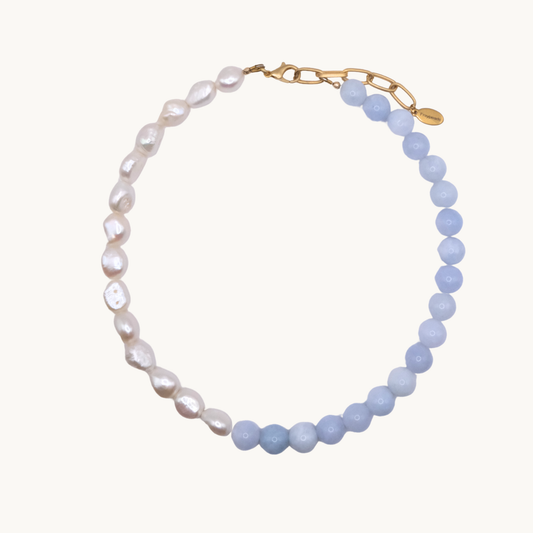 A necklace featuring alternating natural white pearls and smooth blue beads, connected by a gold clasp with a small branded tag. Elegant and stylish.
